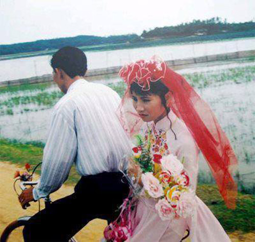 Chú rể đón cô dâu về nhà bằng chiếc xe đạp cũ. Cô dâu đội rế đỏ trên đầu