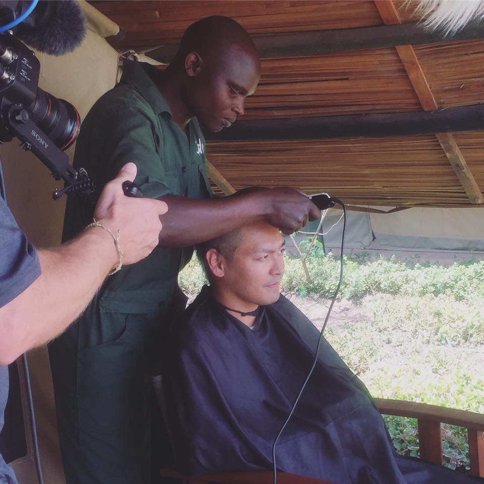 Hình ảnh MC Phan Anh đang được một người dân châu Phi cạo đầu.